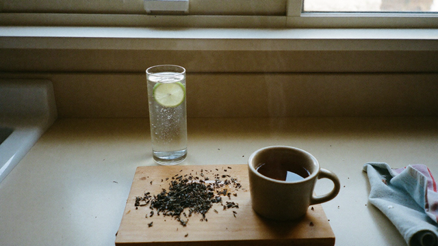 Glass of sparkling water with lime beside a mug of tea and loose-leaf tea