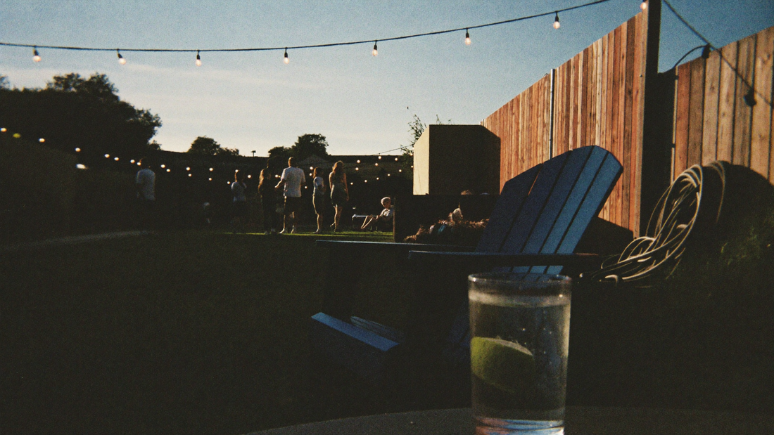 Backyard deck at dusk with string lights and a drink on a chair