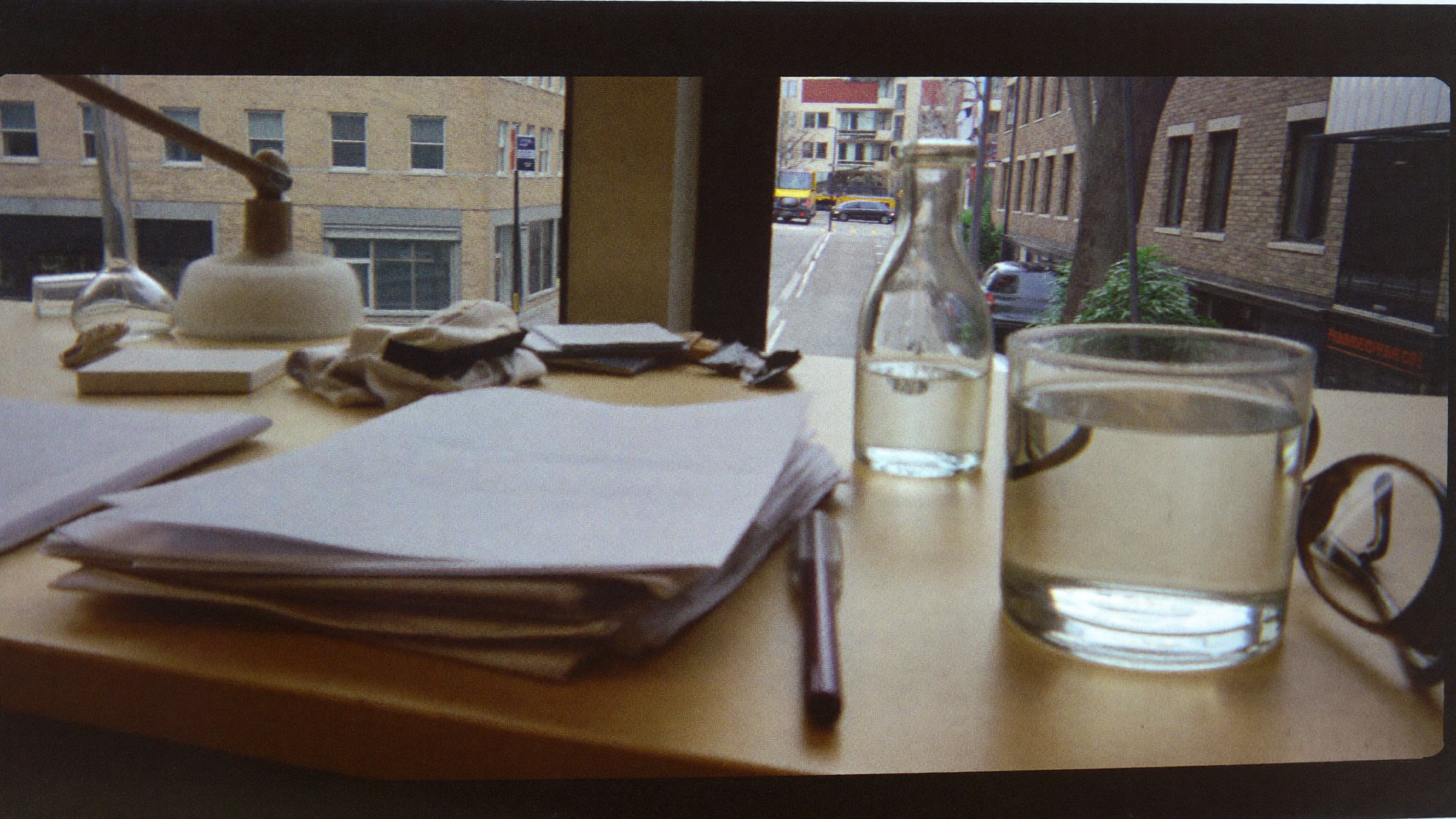 Notebook, bottle, and glass of water on a desk by a window