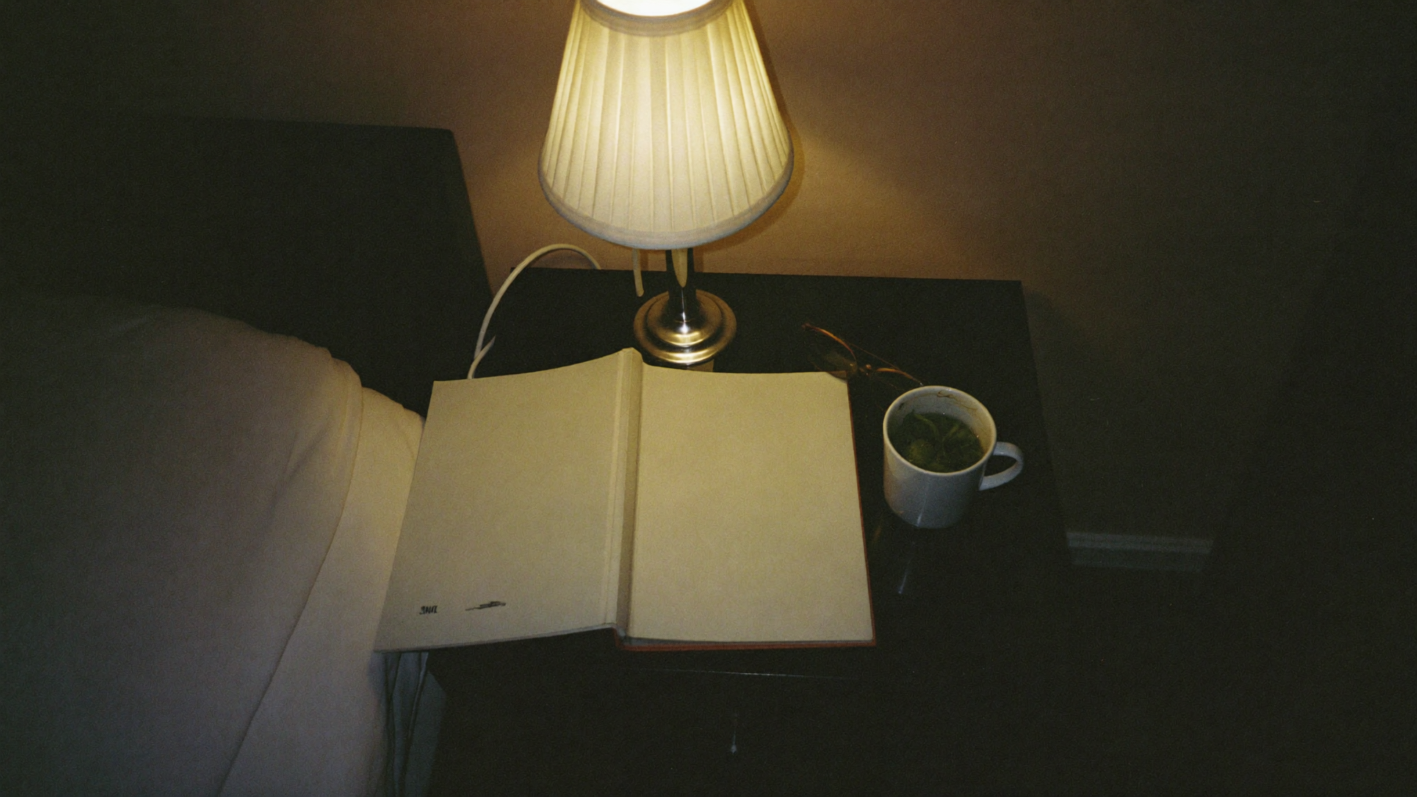 Bedside table at night with a lamp, open notebook, and mug